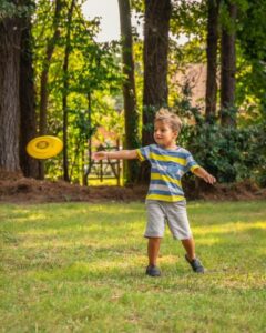 little boy throwing a frisbee in his front yard